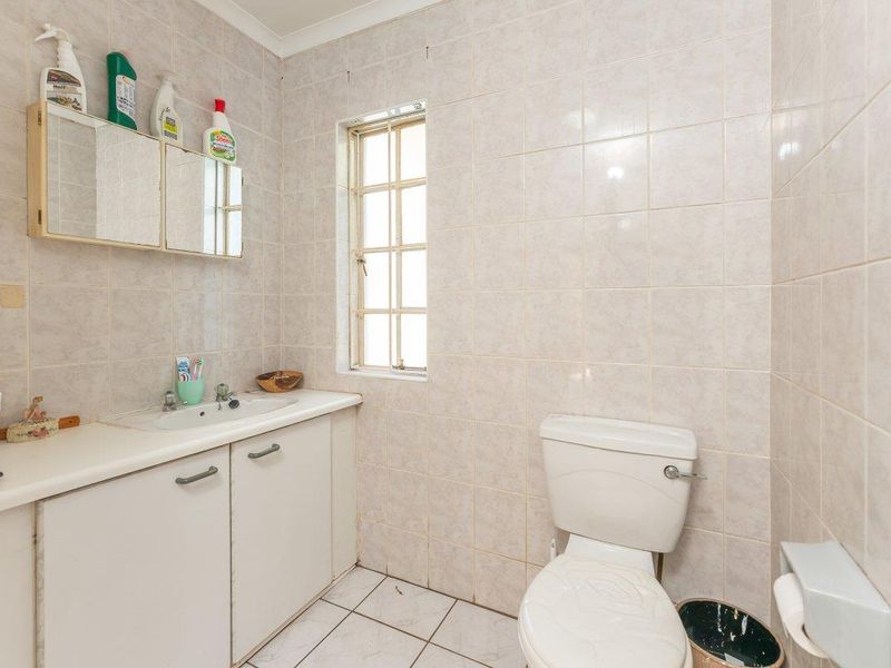 A dated bathroom featuring tiled walls and flooring, a built-in vanity cabinet with a basin, and a standard toilet.