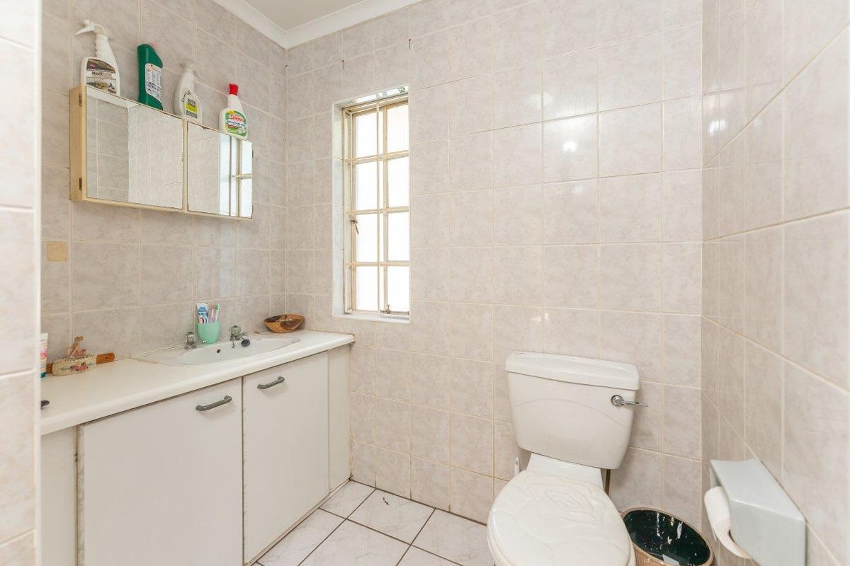 A dated bathroom featuring tiled walls and flooring, a built-in vanity cabinet with a basin, and a standard toilet.
