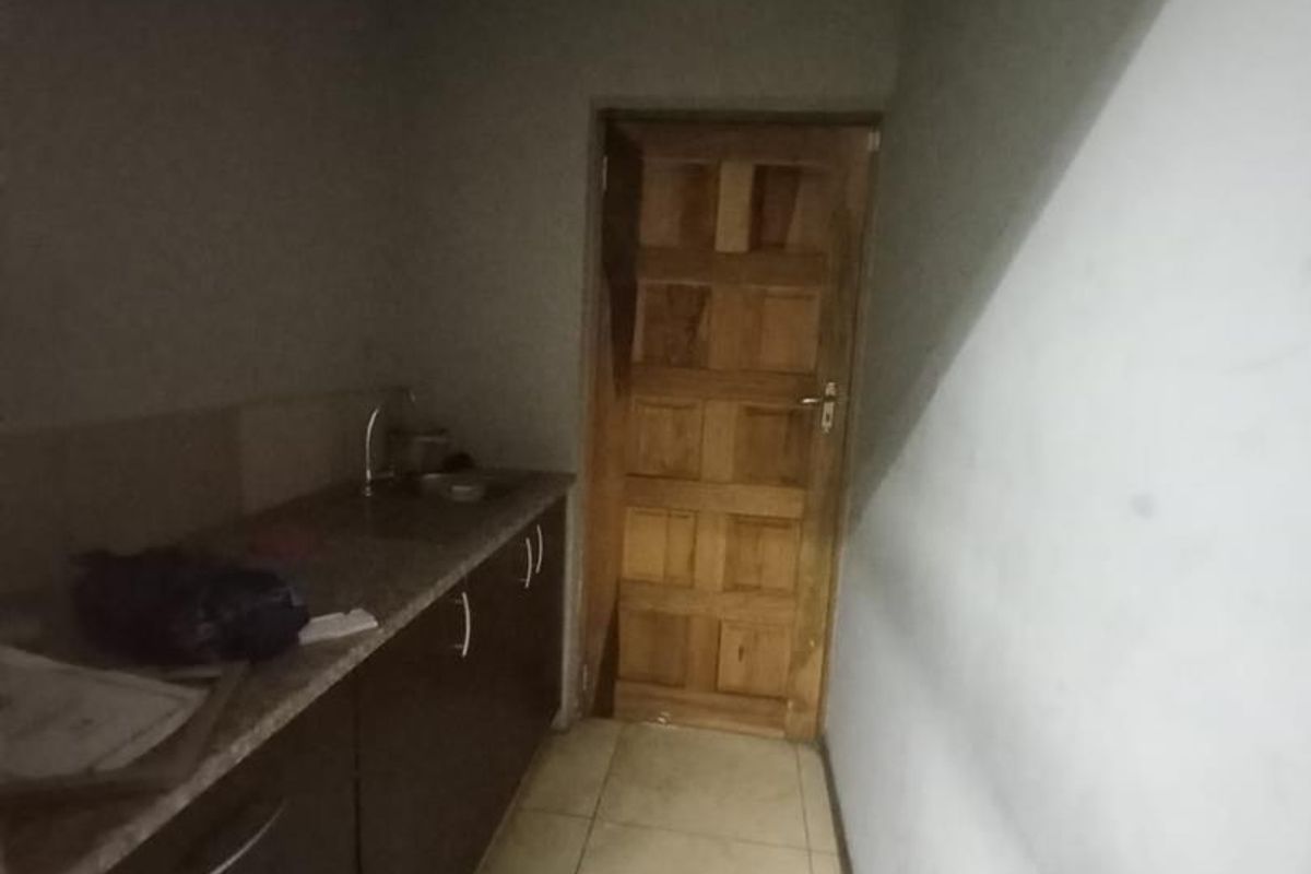 A functional scullery or utility area featuring built-in cabinetry, a granite countertop with a sink, and tiled flooring.