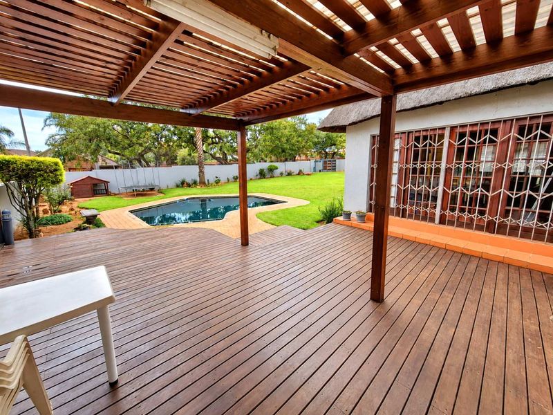 Spacious wooden deck with a pergola, overlooking a private swimming pool and landscaped garden area.