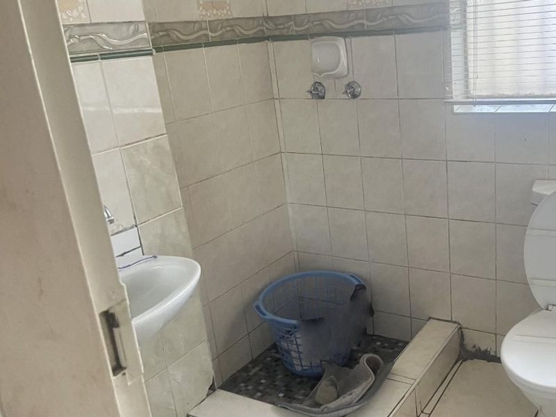 A compact bathroom featuring a wall-mounted basin, toilet, and tiled finishes, currently requiring some maintenance and cosmetic updates to the flooring and tile work.