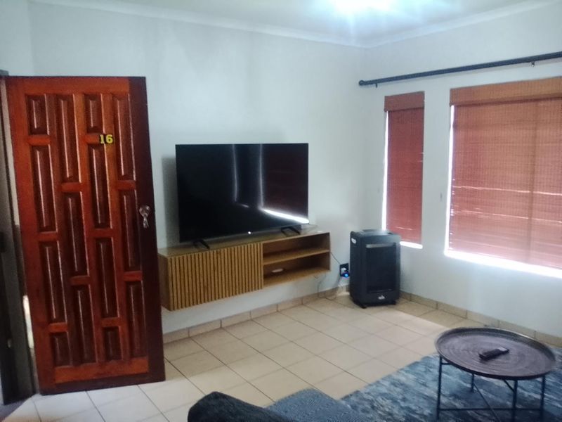 A living room featuring tiled flooring, a floating media console, and wooden blinds, providing a functional and neutral space.