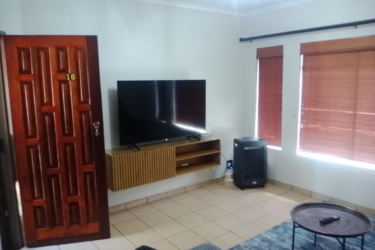 A living room featuring tiled flooring, a floating media console, and wooden blinds, providing a functional and neutral space.