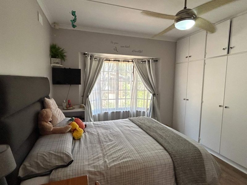 A well-maintained bedroom featuring extensive built-in cupboards, a ceiling fan, and a charming bay window that allows for natural light.