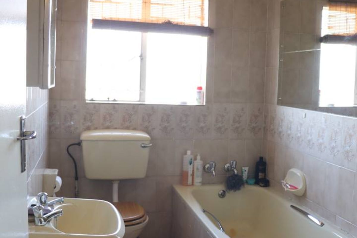 A dated bathroom featuring a pedestal basin, a standard toilet, and a tiled bathtub with wall-mounted mirror and window.