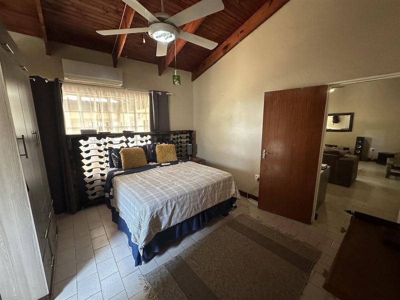 A bedroom featuring a vaulted timber ceiling, ceiling fan, split-system air conditioner, and tiled flooring with an adjacent room visible through the doorway.