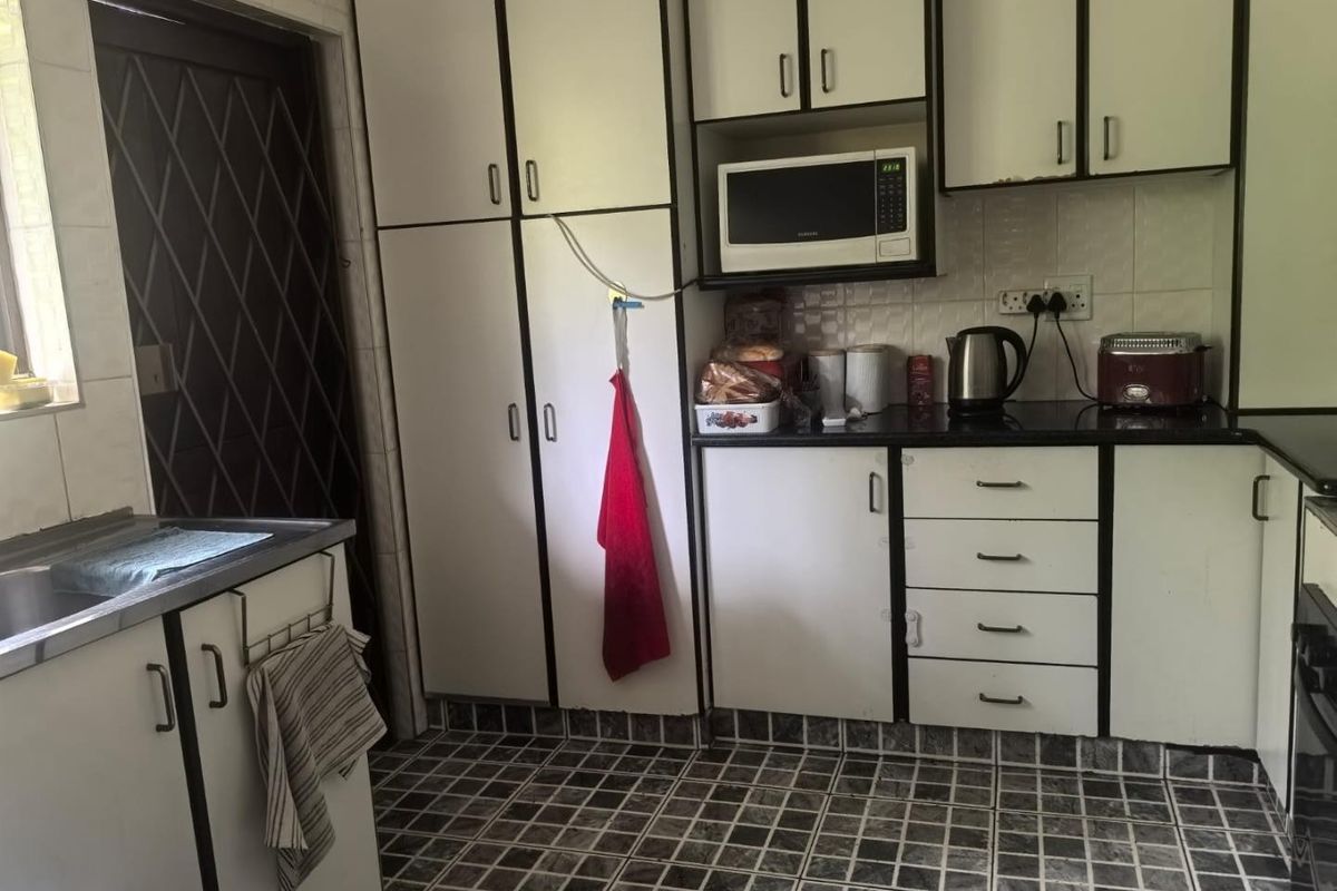 A functional kitchen featuring white built-in cabinetry, dark countertops, a built-in microwave, and tiled flooring, offering a practical layout for daily meal preparation.