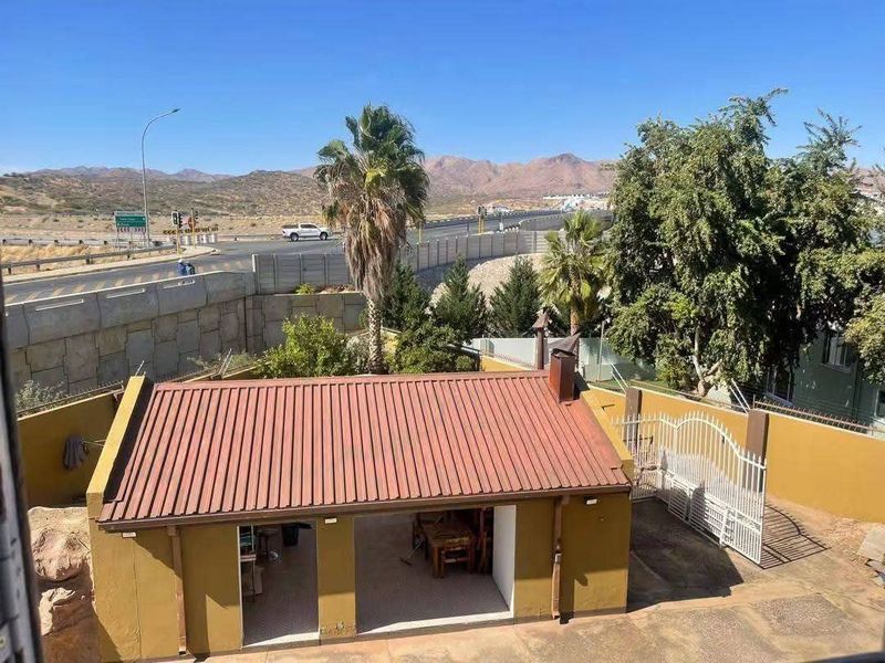 Elevated view of a rear courtyard featuring a detached structure with a corrugated metal roof, outdoor fireplace, and secure perimeter fencing.
