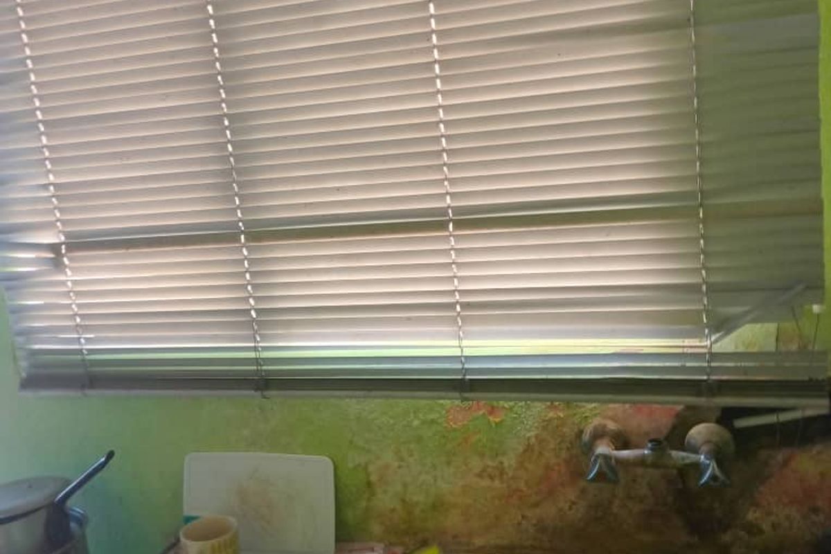 A kitchen sink area featuring a stainless steel basin and faucet, currently showing significant wall surface deterioration and peeling paint.