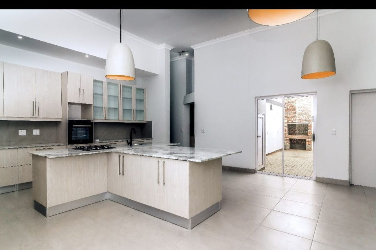 Modern open-plan kitchen featuring light wood cabinetry, stone countertops, and integrated appliances, flowing seamlessly to an outdoor patio area.