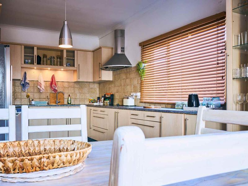 A functional kitchen featuring light wood-tone cabinetry, tiled backsplash, stainless steel extractor fan, and ample counter space with natural light from the window.