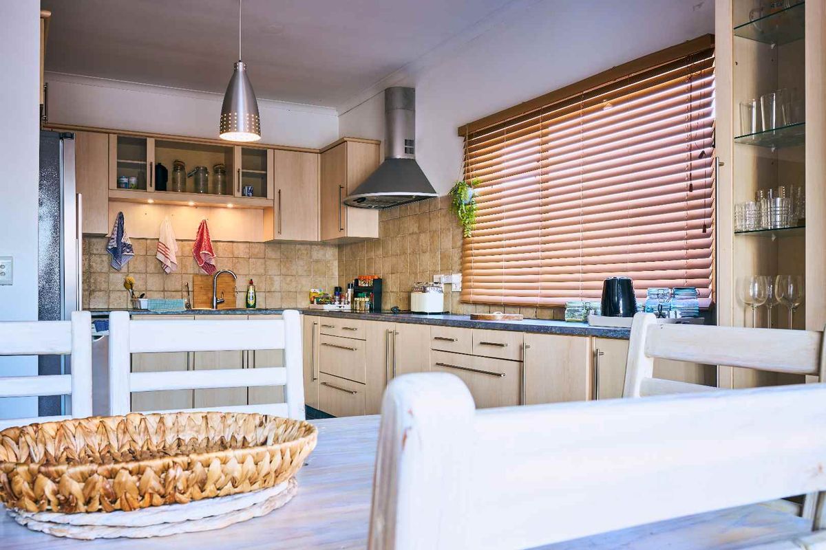 A functional kitchen featuring light wood-tone cabinetry, tiled backsplash, stainless steel extractor fan, and ample counter space with natural light from the window.