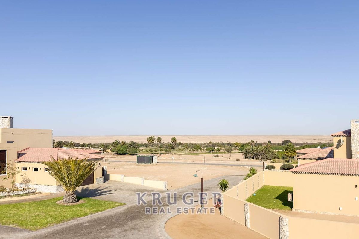 Aerial view of a residential property complex featuring paved driveways, boundary walls, and tiled roof structures set against a desert landscape.