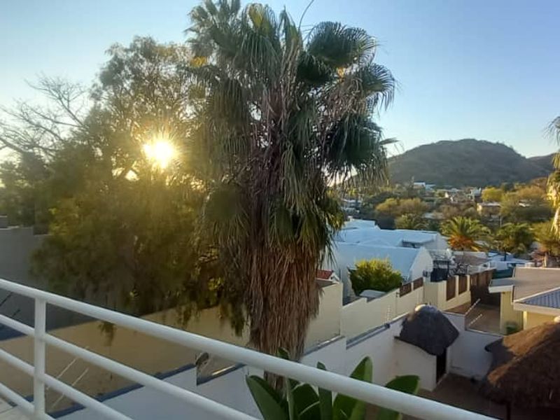 An elevated balcony featuring a white metal balustrade, offering scenic views of the surrounding neighbourhood and mature palm trees.