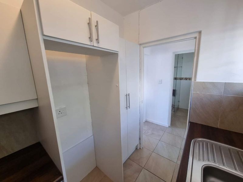 A clean, functional kitchen area featuring white built-in cabinetry, laminate countertops, and a stainless steel sink, with tiled flooring throughout.