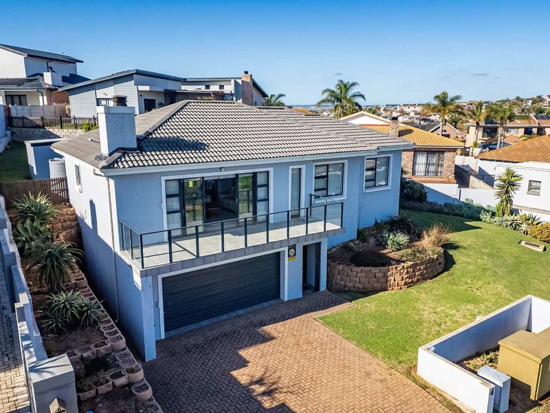 Elevated view of a modern two-story house featuring a tiled roof, balcony with glass balustrade, double garage, and a well-maintained garden.