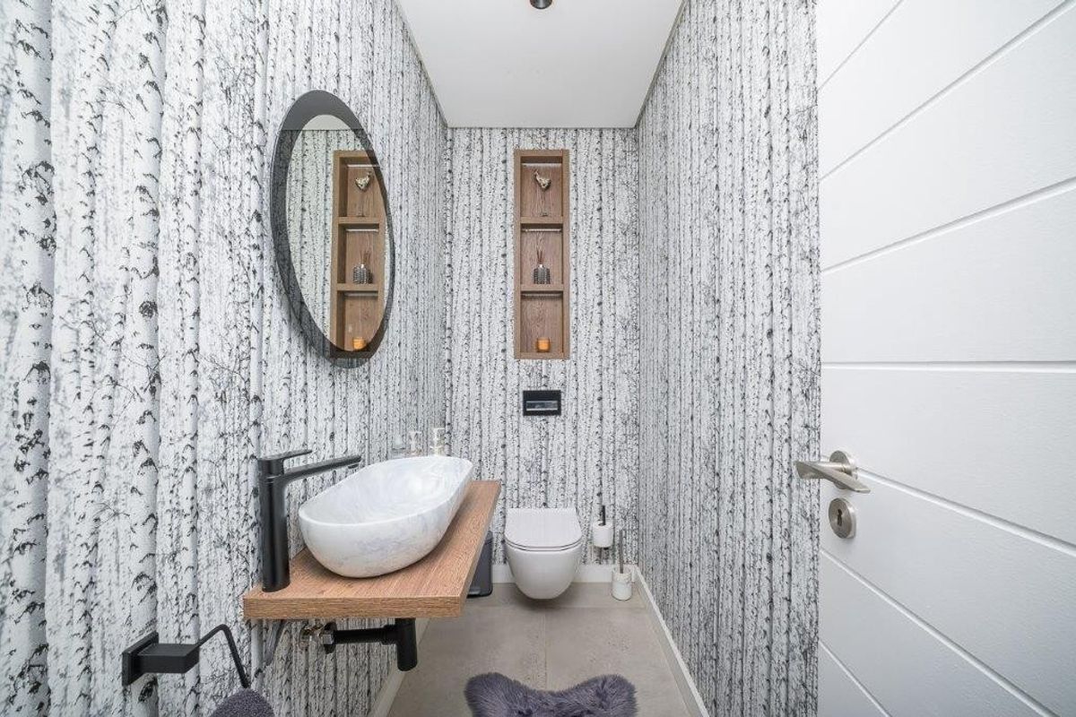 Modern guest bathroom featuring a floating vanity shelf, vessel sink, wall-mounted toilet, and unique patterned wallpaper with recessed shelving.