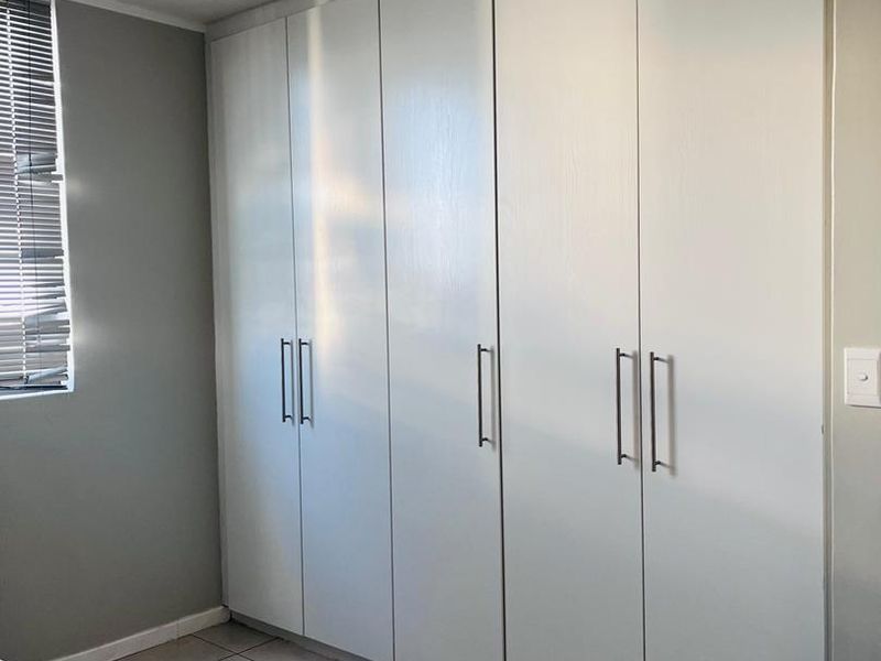 A bedroom featuring neutral tiled flooring, grey walls, and a large wall-to-wall built-in cupboard unit with modern handles.
