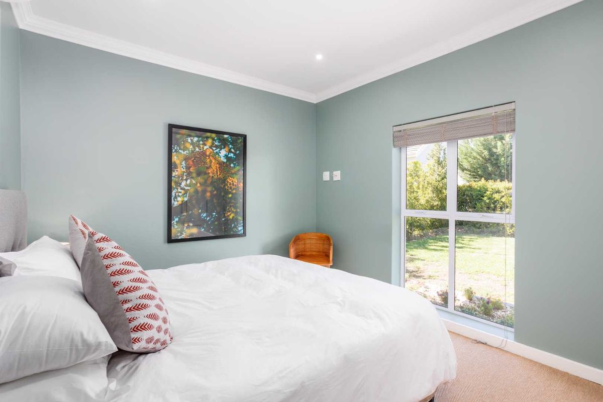 A well-maintained bedroom featuring soft green walls, neutral carpeting, and a large window providing natural light and garden views.
