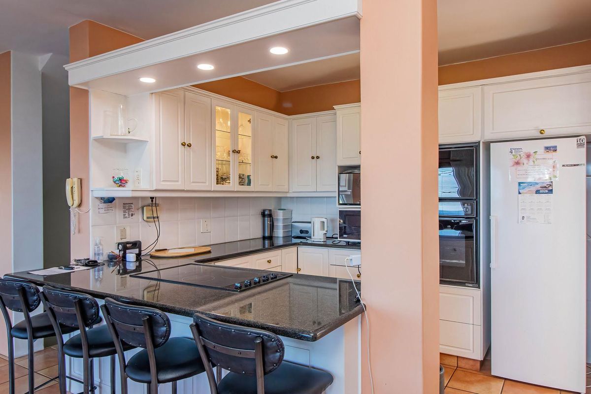 A functional kitchen featuring white cabinetry, dark granite countertops, a breakfast bar, and built-in oven and microwave units.
