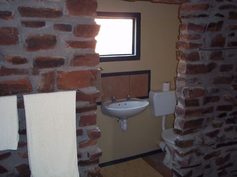 A rustic bathroom featuring exposed stone wall accents, a wall-mounted basin, and a standard close-coupled toilet.