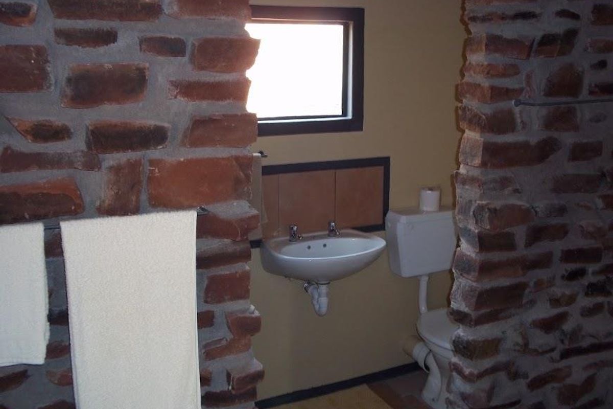 A rustic bathroom featuring exposed stone wall accents, a wall-mounted basin, and a standard close-coupled toilet.