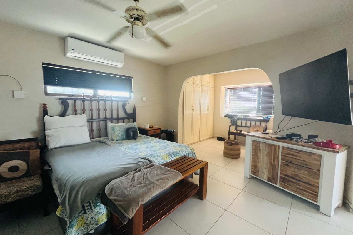 Spacious bedroom featuring tiled flooring, a ceiling fan, wall-mounted air conditioning unit, and an arched entryway leading to a built-in wardrobe area.