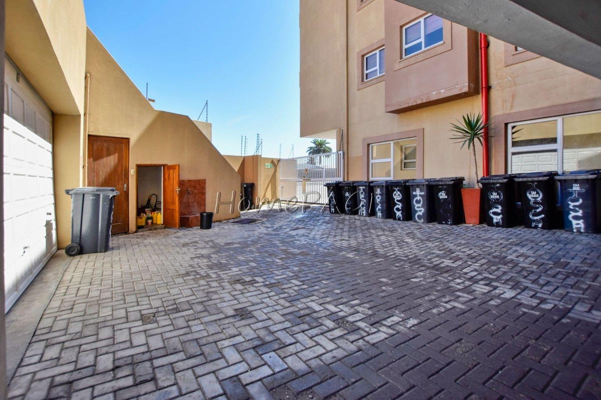 A paved exterior courtyard area featuring a garage entrance, utility access, and perimeter walling within an apartment complex.