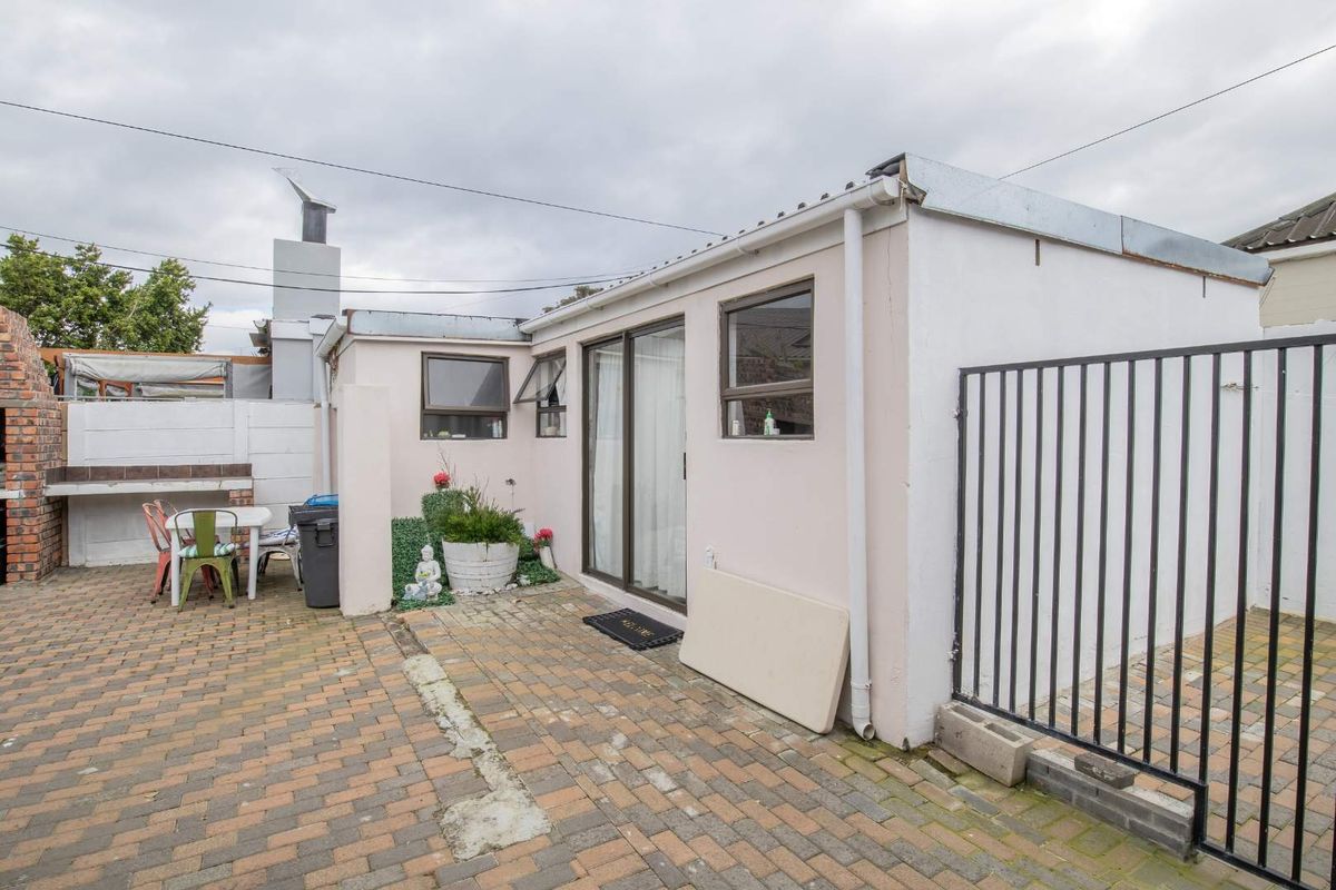 Rear exterior view featuring a paved courtyard, built-in brick braai area, and sliding door access to the main dwelling.