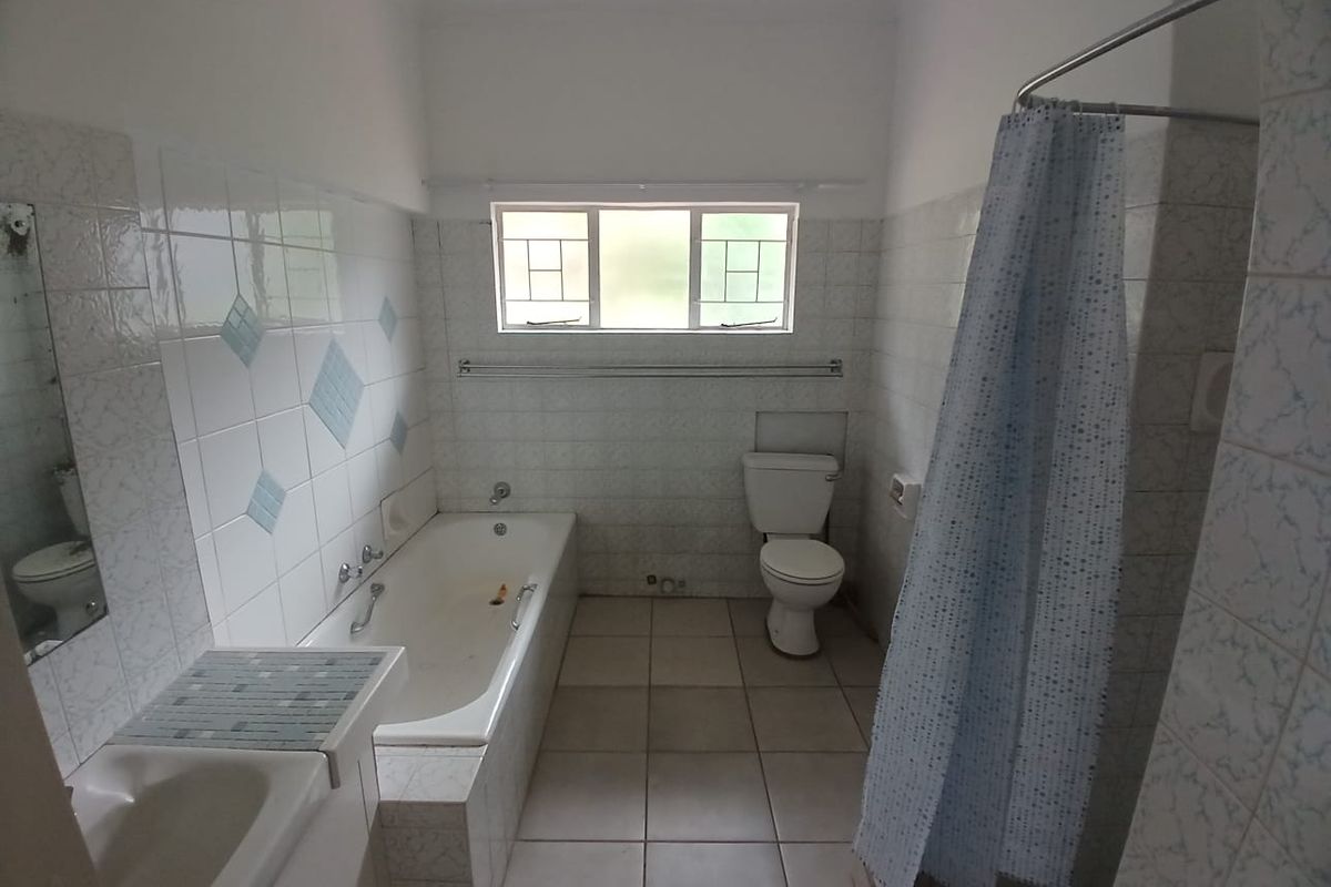 A dated bathroom featuring a built-in bathtub, a separate shower area with a curtain, a toilet, and a vanity basin with tiled finishes.