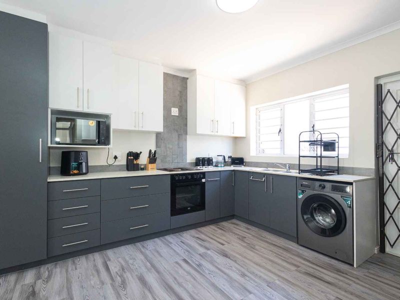 Modern kitchen featuring two-tone cabinetry, integrated appliances, laminate flooring, and a security gate leading to the exterior.