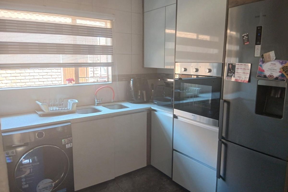 Compact kitchen featuring modern cabinetry, built-in oven, double sink, and dedicated space for laundry appliances under the counter.
