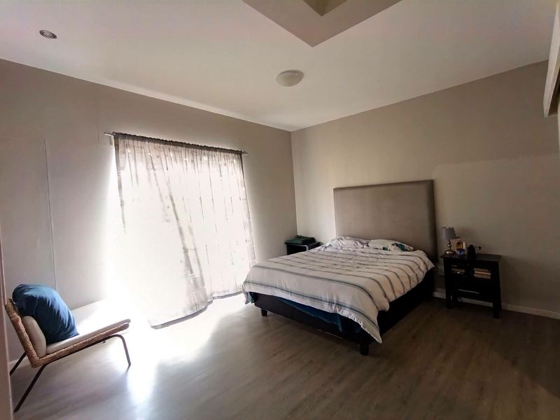 A well-lit bedroom featuring laminate flooring, a recessed ceiling detail, and a sliding glass door providing natural light.