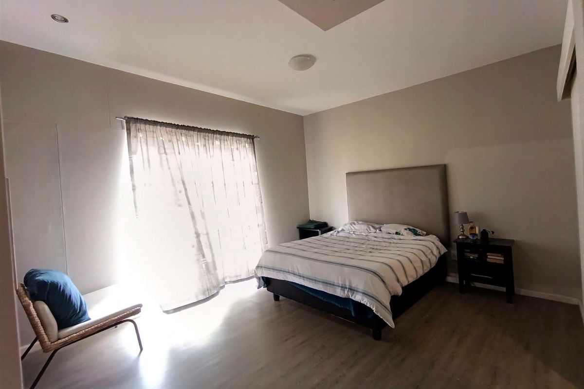 A well-lit bedroom featuring laminate flooring, a recessed ceiling detail, and a sliding glass door providing natural light.