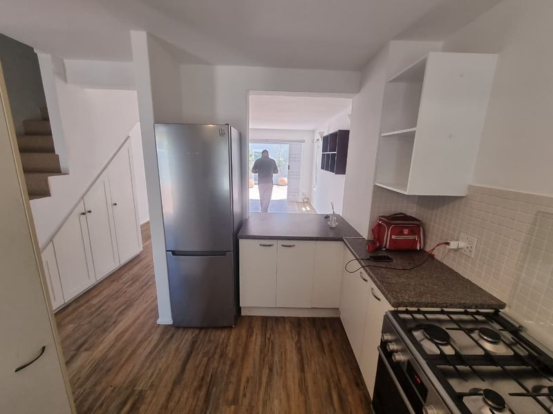 Compact kitchen featuring white cabinetry, laminate countertops, gas stove, and tiled backsplash, with convenient under-stair storage and direct access to the living area.