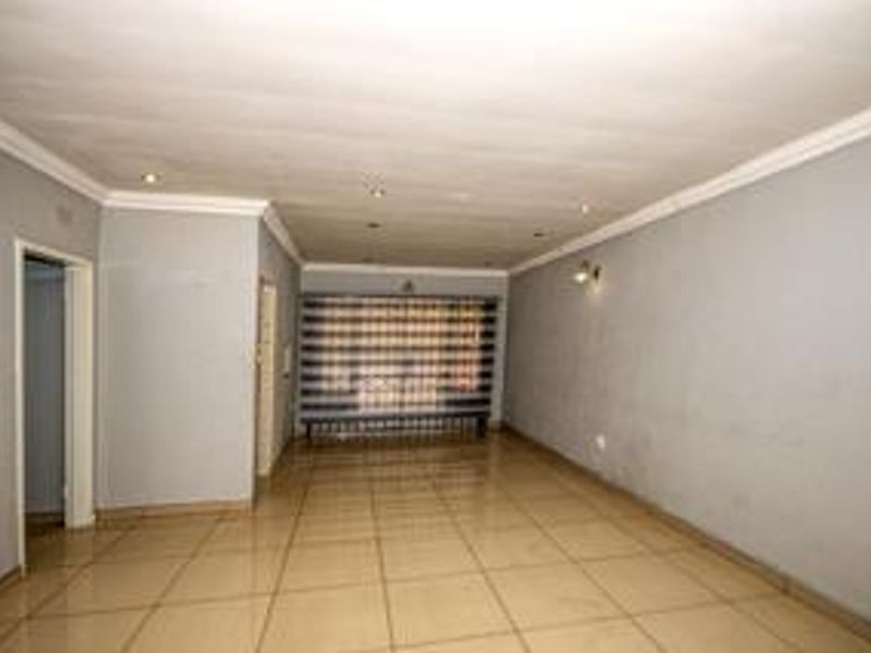 A spacious, empty living area featuring neutral tiled flooring, recessed lighting, and a secure window gate, offering a blank canvas for interior design.