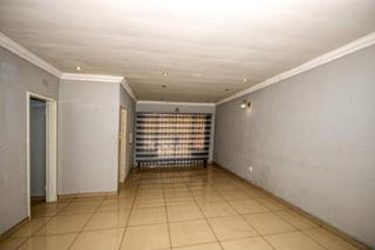 A spacious, empty living area featuring neutral tiled flooring, recessed lighting, and a secure window gate, offering a blank canvas for interior design.