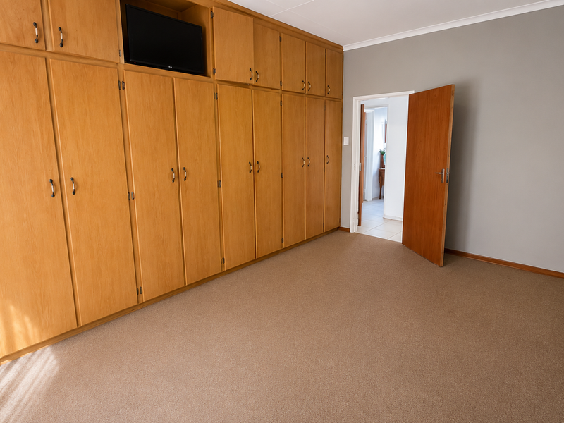 A spacious bedroom featuring extensive wall-to-wall built-in wooden cupboards and neutral carpeting, offering a clean and functional living space.