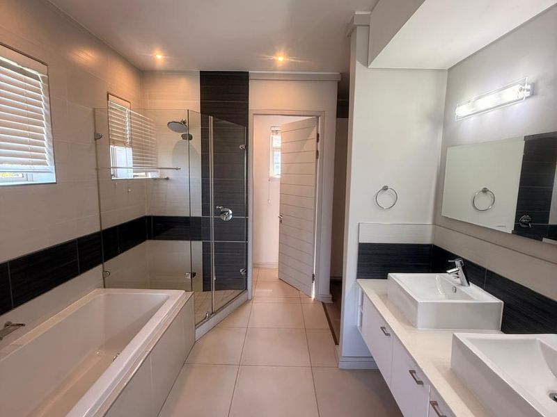 Modern bathroom featuring a double vanity with vessel sinks, a built-in bathtub, and a separate glass-enclosed shower with contemporary tile finishes.