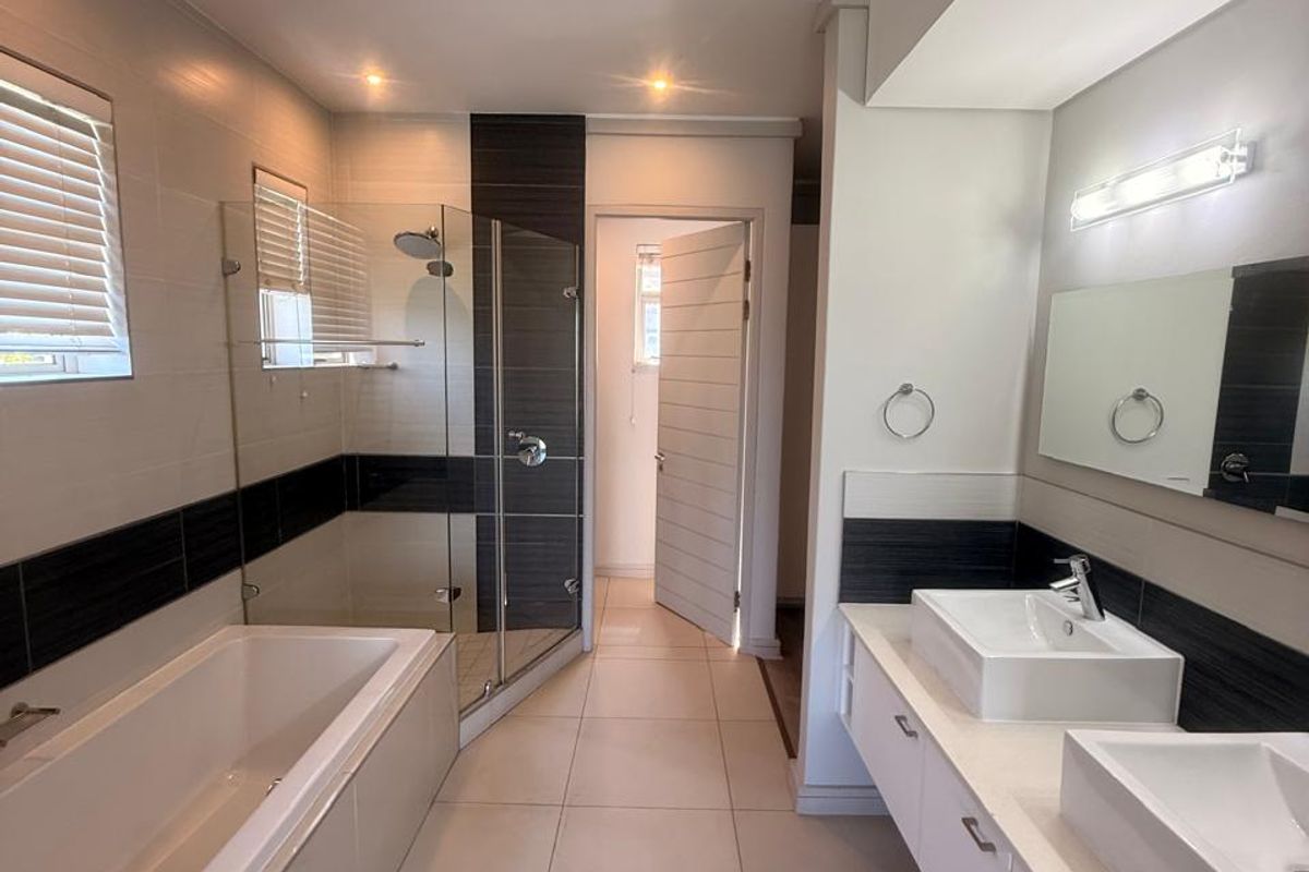 Modern bathroom featuring a double vanity with vessel sinks, a built-in bathtub, and a separate glass-enclosed shower with contemporary tile finishes.