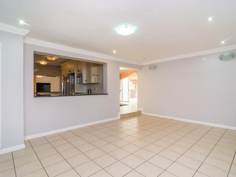 An open-plan living area featuring tiled flooring, recessed ceiling lighting, and a service window connecting to the kitchen space.