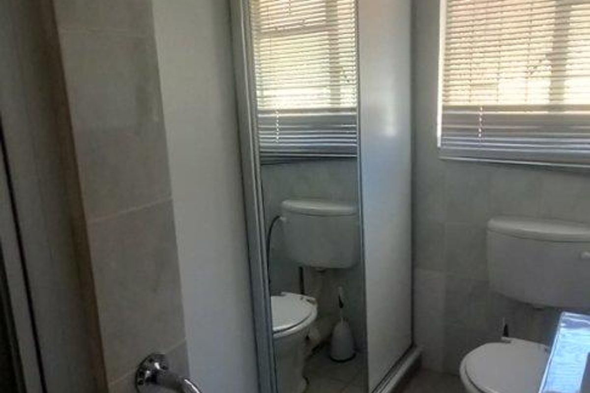 A functional bathroom featuring a toilet, vanity, and sliding mirror doors, with tiled flooring and a window fitted with blinds.