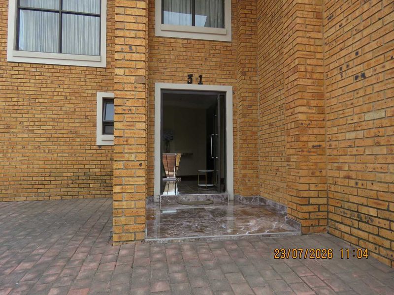 Front entrance of a face-brick cluster home featuring a paved driveway and tiled entrance landing.