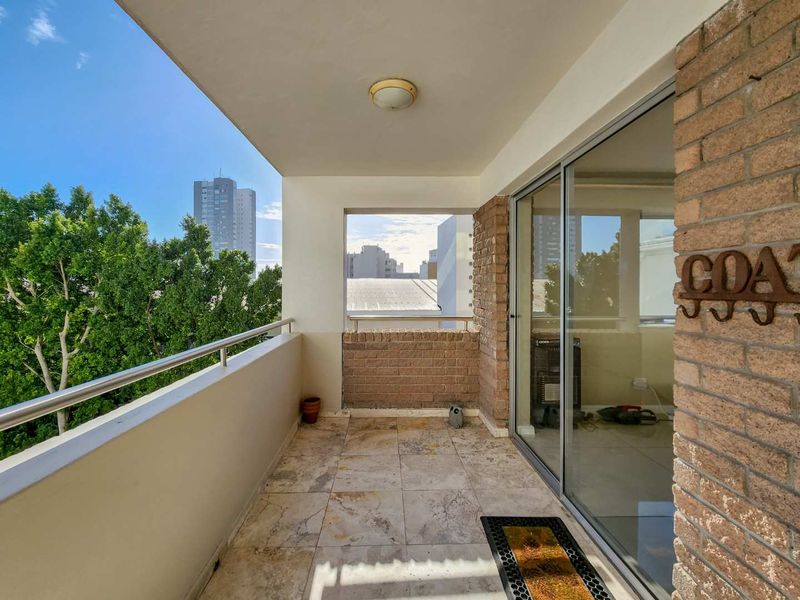 A covered balcony featuring stone tile flooring, a brick feature wall, and a metal balustrade, offering an open-air space with urban views.