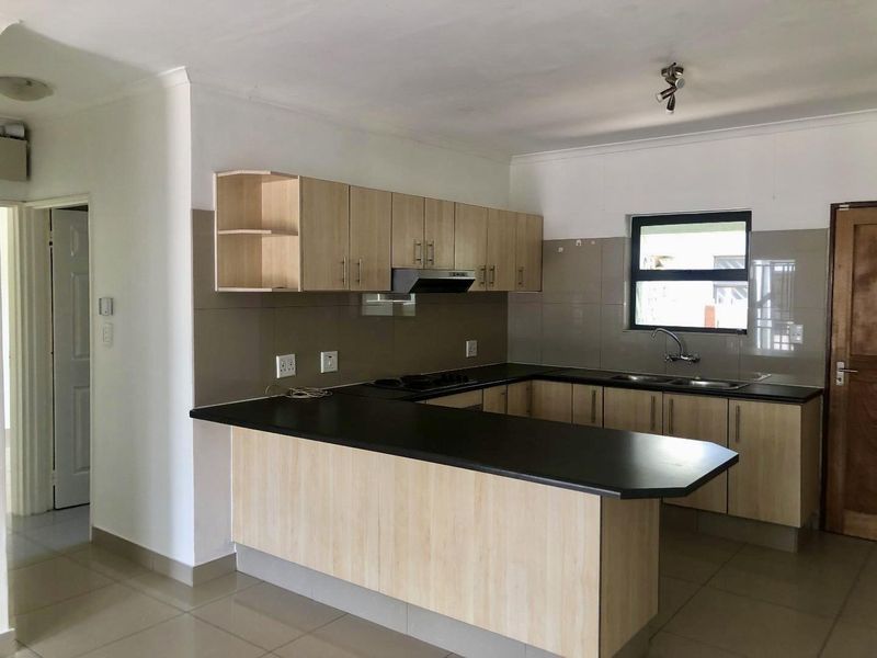 A clean, functional kitchen featuring light wood-finish cabinetry, dark countertops, a built-in hob with extractor, and a tiled backsplash.