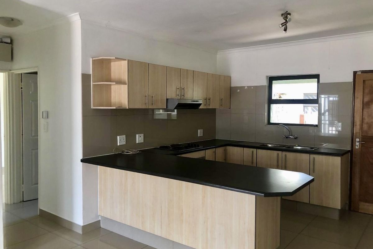 A clean, functional kitchen featuring light wood-finish cabinetry, dark countertops, a built-in hob with extractor, and a tiled backsplash.