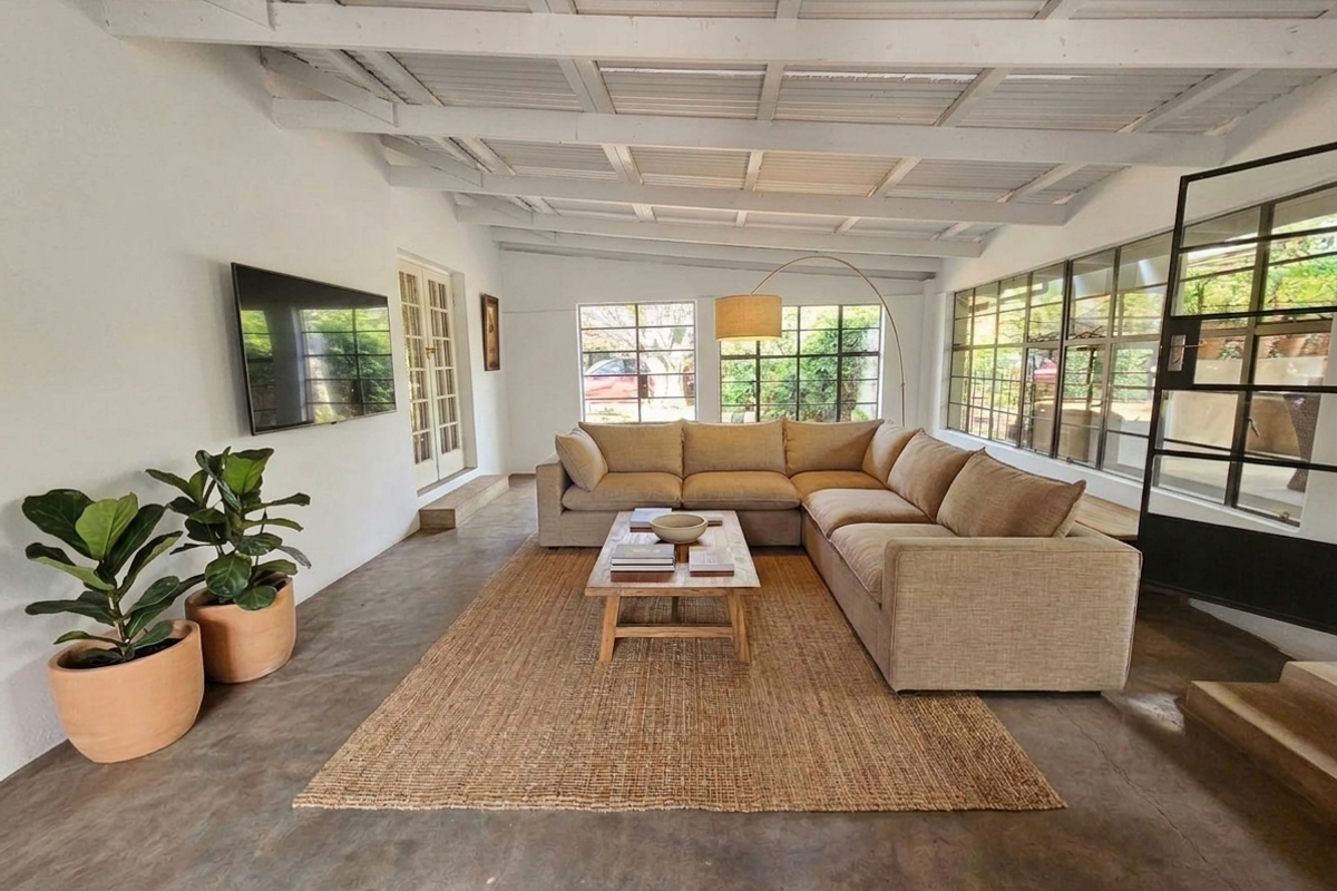 Spacious living area featuring exposed beam ceilings, polished concrete flooring, and large steel-framed windows providing ample natural light.