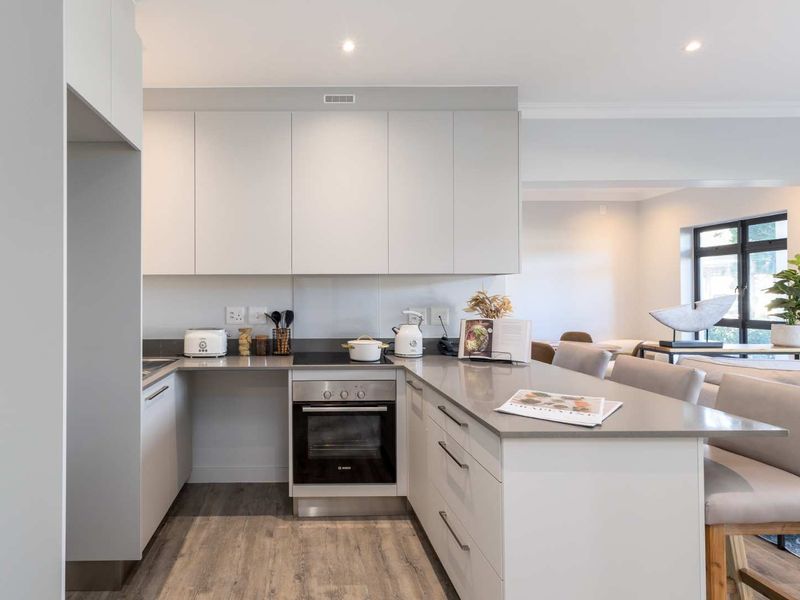 Modern open-plan kitchen featuring sleek white cabinetry, stone countertops, integrated oven and hob, and durable laminate flooring, seamlessly flowing into the living area.