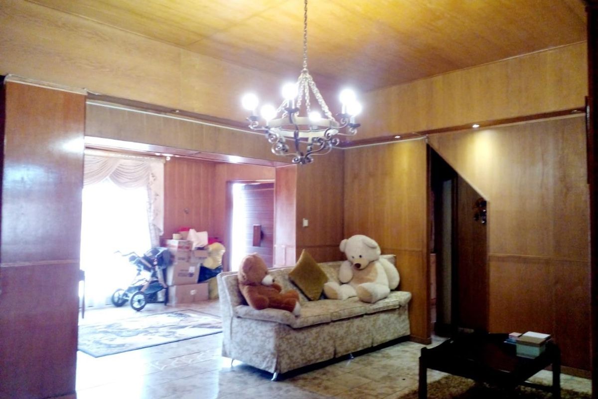 Spacious living area featuring extensive wood paneling, tiled flooring, and a central chandelier, offering a dated aesthetic with potential for modernization.