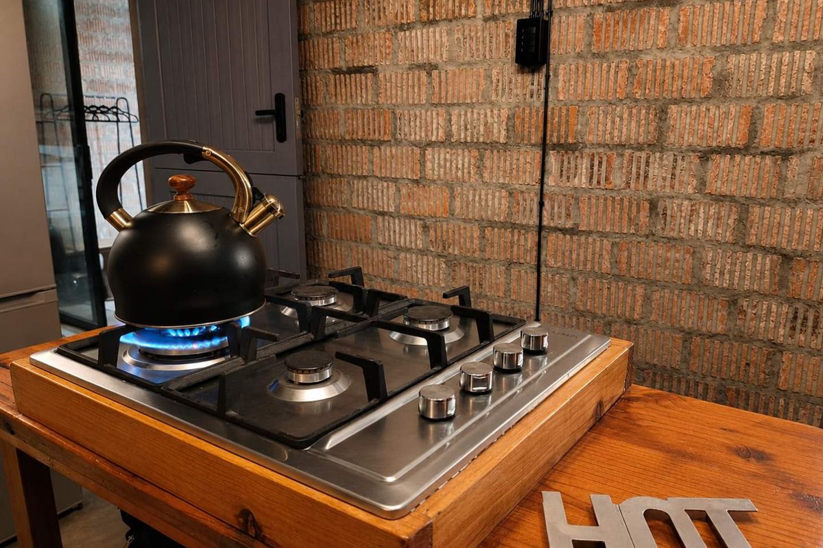 A close-up view of a stainless steel gas cooktop set into a timber countertop against an exposed brick wall.